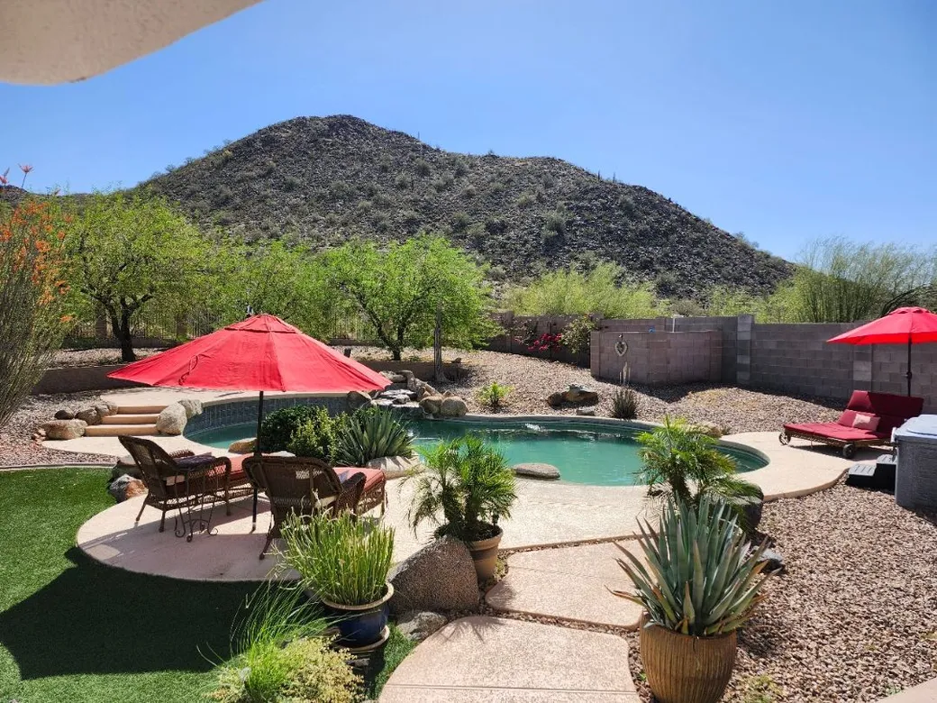 The pool, with red umbrellas, lounge chairs and a desert hill behind