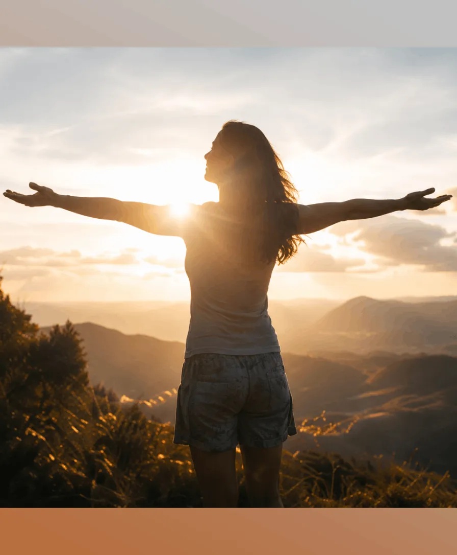 A woman with open arms facing a desert sunset